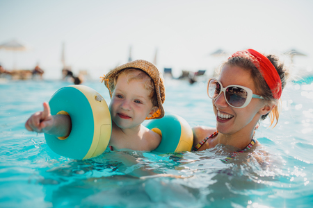A small toddler boy with armbands and mother swimming in water on summer holiday.の写真素材