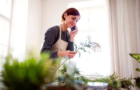 Young creative woman in a flower shop, using smartphone. A startup of florist business.の写真素材