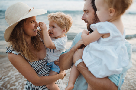 A young family with two toddler children standing on beach on summer holiday.の写真素材