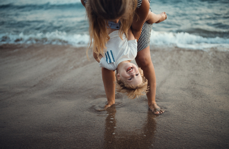 Young mother with a toddler boy standing on beach on summer holiday, having fun.の写真素材