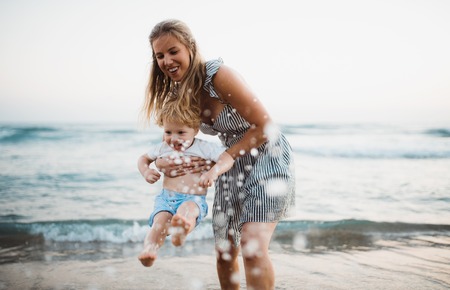 Young mother with a toddler boy standing on beach on summer holiday, having fun.の写真素材