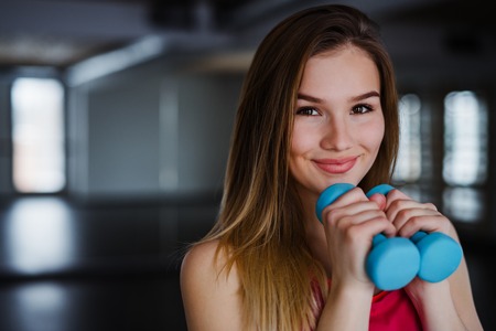 A portrait of young girl or woman with dumbbells in a gym. Copy space.の写真素材