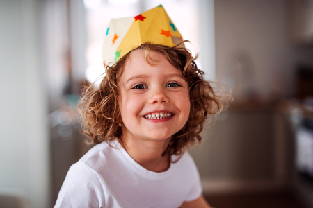 A small girl with a paper crown at home, looking at camera.の写真素材