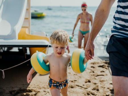 Family with two small toddler children walking on beach on summer holiday.