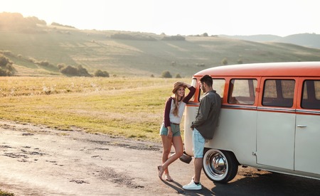 A young couple on a roadtrip through countryside, standing by minivan.