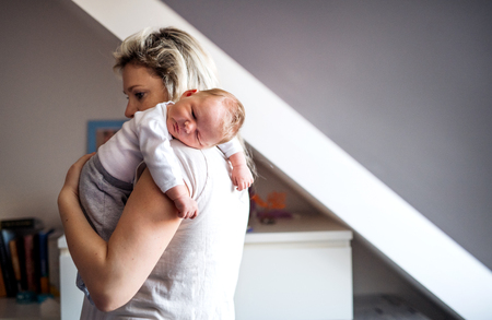 A beautiful young mother with a sleeping newborn baby at home. Copy space.の写真素材