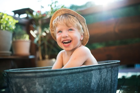 Small boy with a hat in bath outdoors in garden in summer, playing in water.の写真素材