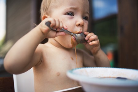 Small girl standing by a table on a patio in summer, eating soup.の写真素材