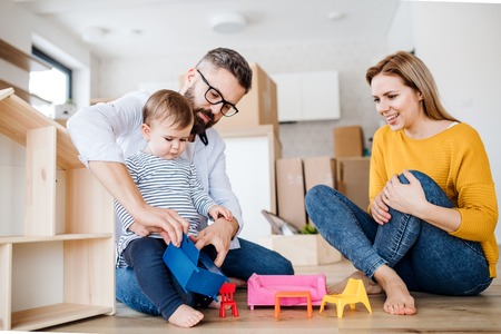 A portrait of young family with a toddler girl moving in new home, playing.