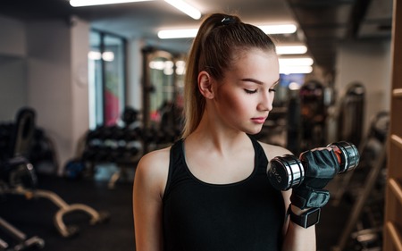 Young girl or woman with dumbbells, doing workout in a gym.の写真素材