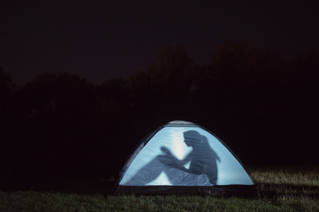 A silhouette of a girl sitting in a tent outdoors at night.の写真素材