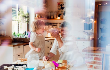 Senior grandmother with small toddler boy making cakes at home.の写真素材