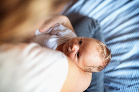 A midsection of mother with a newborn baby at home.