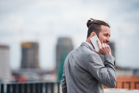 A young businessman with smartphone standing on a terrace, making a phone call.の写真素材