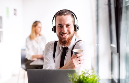 A portrait of young businessman with headphones and coffee in an office.の写真素材