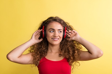 Portrait of a young woman with headphones in a studio on a yellow background.の写真素材