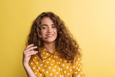 Portrait of a young woman with glasses in a studio on a yellow background.
