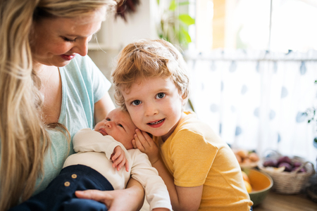A beautiful young mother with a newborn baby and his brother at home.の写真素材