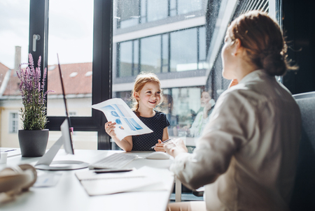 A businesswoman with small daughter sitting in an office, working.の写真素材