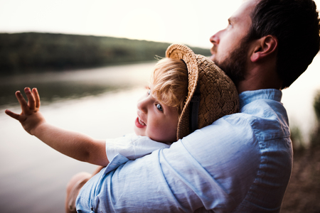 Mature father with a toddler boy outdoors by the river in summer.の写真素材