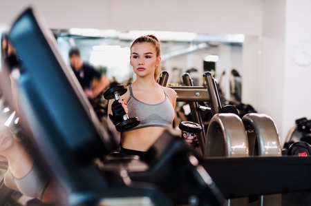 Young girl or woman with dumbbells, doing workout in a gym.