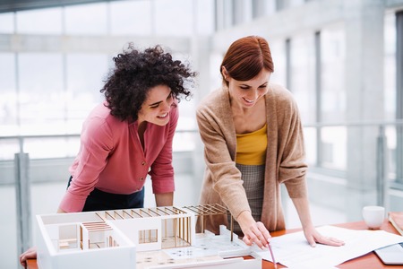 Female young architects with model of a house standing in office, talking.の写真素材