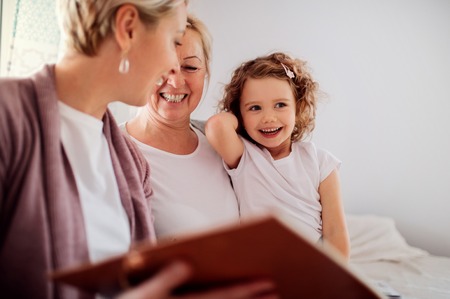 A small girl with mother and grandmother at home, looking at photographs.の写真素材