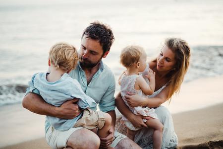 A family with two toddler children sitting on sand beach on summer holiday.の写真素材