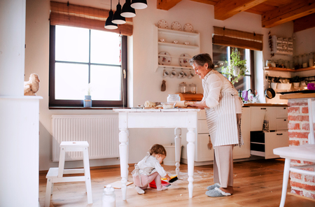 Senior grandmother with small toddler grandchild making cakes at home.の写真素材