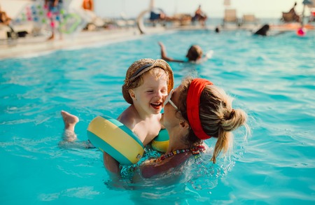A small toddler boy with armbands and mother swimming in water on summer holiday.の写真素材