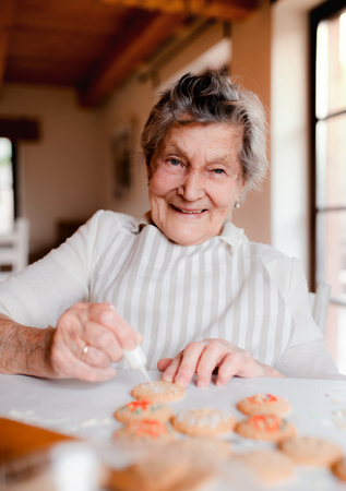 Elderly woman making and decorating cakes in a kitchen at home.の写真素材