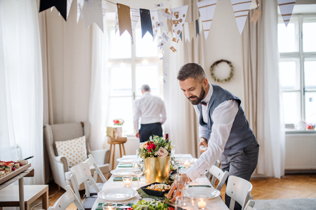 A portrait of a senior and mature man standing indoors in a room set for a party.の写真素材