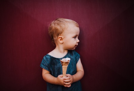 A front view of small toddler girl outdoors in summer, eating ice cream.の写真素材
