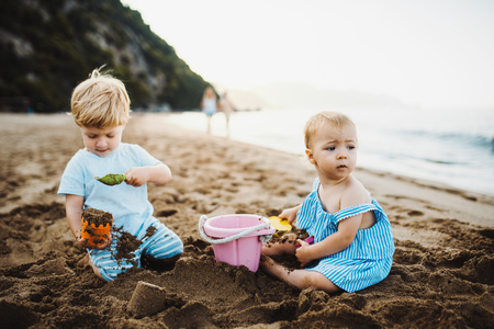 Two toddler children playing on sand beach on summer holiday.