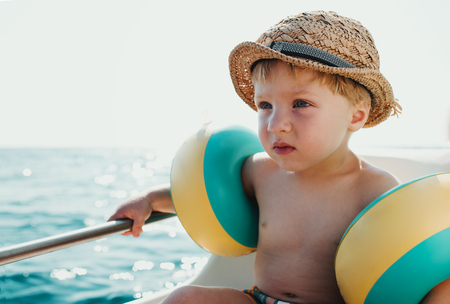 A small boy with armbands sitting on boat on summer holiday.の写真素材