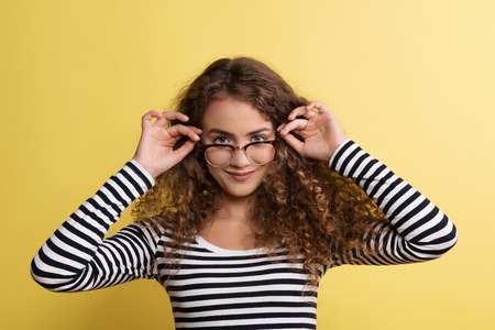 Portrait of a young woman with glasses in a studio on a yellow background.