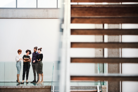 Group of young businesspeople standing near staircase, talking.の写真素材