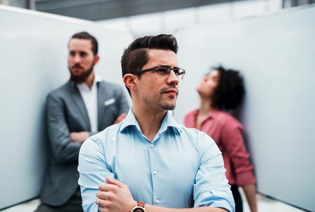 A young businessman standing in office, colleagues in the background.の写真素材