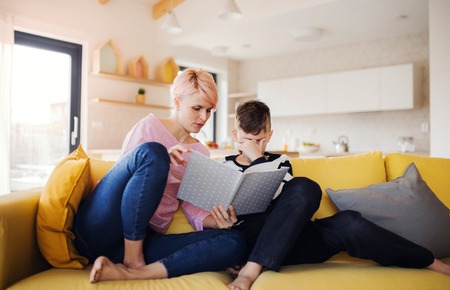 A young woman with a son indoors at home, reading a book.の写真素材