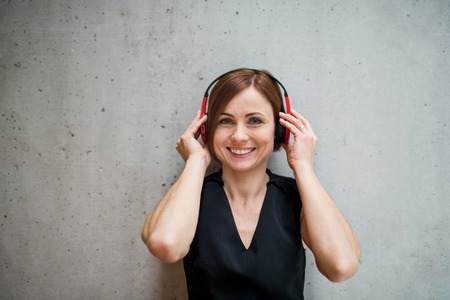 Young business woman with headphones standing against concrete wall in office.の写真素材