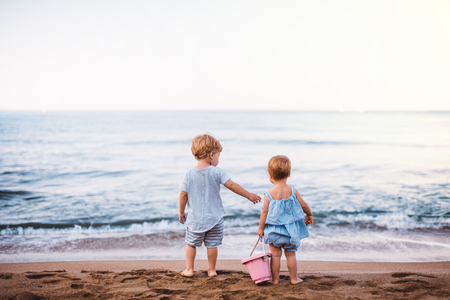Rear view of two toddler children playing on sand beach on summer holiday.の写真素材
