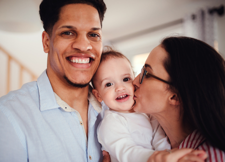 Portrait of young family with small toddler son indoors at home, kissing.の写真素材