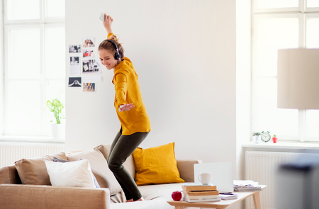 A young female student with headphones dancing on sofa when studying.の写真素材