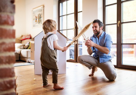 A toddler boy and father with carton swords playing indoors at home.の写真素材