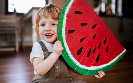A toddler boy playing with large toy fruit indoors at home.の写真素材