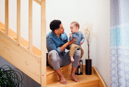 A portrait of father and small toddler son indoors at home, sitting on staircase.の写真素材
