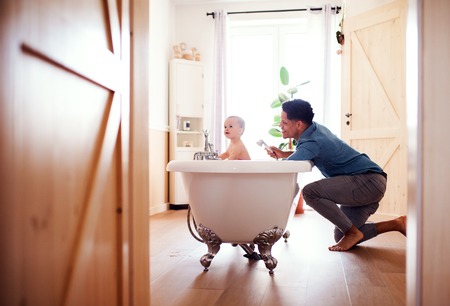 Father washing small toddler son in a bathroom indoors at home.の写真素材