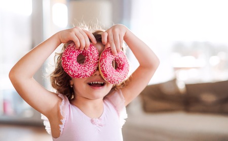 A small girl with doughnuts at home, having fun.の写真素材