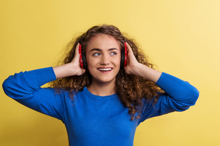 Portrait of a young woman with headphones in a studio on a yellow background.の写真素材