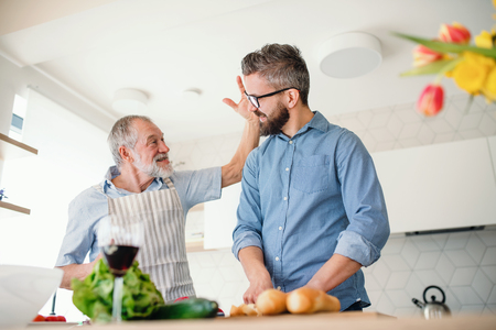 An adult hipster son and senior father indoors at home, preparing food.の写真素材